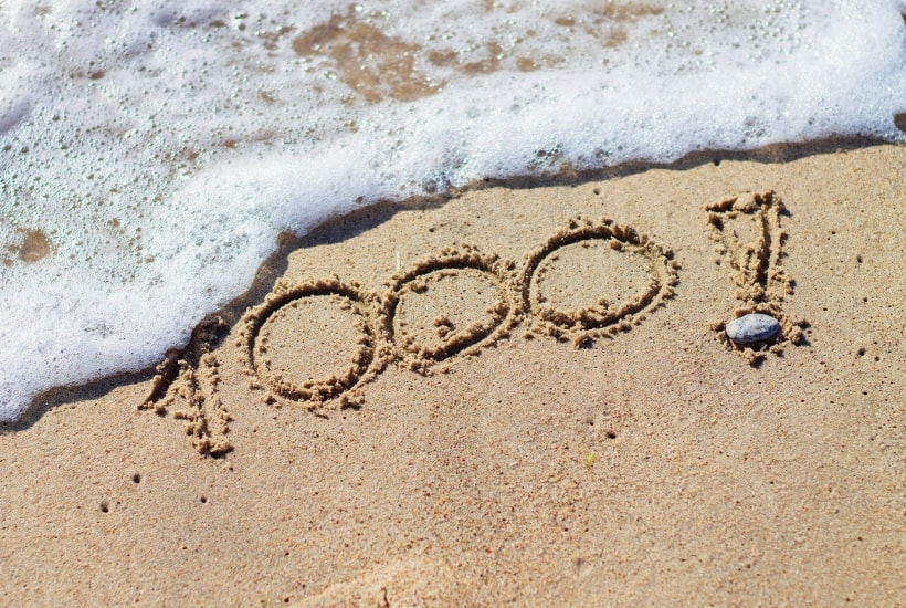 1000! выгравировано на песке с приходом океанской волны, символизирующей планирование дивидендов в размере 1000 долларов в месяц.